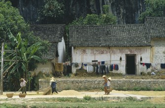 CHINA, Guangxi Province, People drying grain outside a farmhouse.