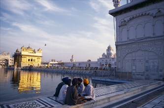 INDIA, Punjab, Amritsar , Group of Sikh men sitting on marble walkway surrounding sacred pool