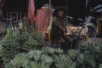 VIETNAM, Nha Trang, Smiling woman sitting behind display of green Bananas
