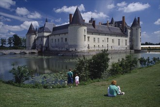 FRANCE, Chateau De Plessey, People sat on the bank of the moat looking towards the chateau.