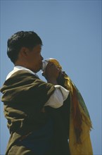 CHINA, Qinghai, Tongren, Tibetan man blowing conch shell at festival