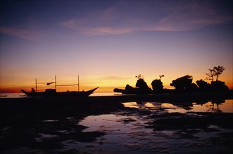 PHILIPPINES, Visayan Islands, Boracay Island, Boat and rocky outcrop silhouetted at sunset