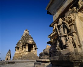 INDIA, Madhya Pradesh, Khajuraho, Vishvanath Temple and carved figures on stone base against blue