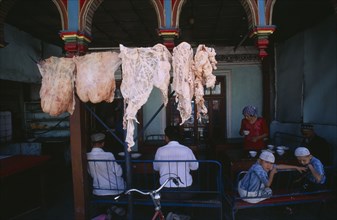 CHINA, Xinjiang, Kashgar, Carcasses of fat hanging outside a restaurant with people sitting at
