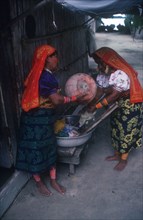 PANAMA, San Blas Island, Cuna Indian women washing clothes with one smoking a pipe