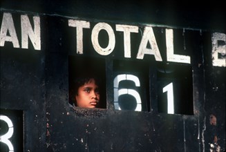 SRI LANKA, Kandy , Young boy peering out through Cricket scoreboard to watch game