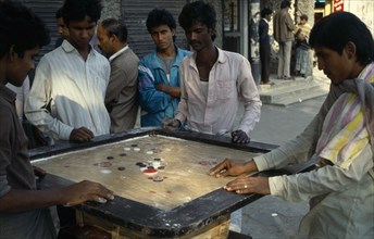 BANGLADESH, Dhaka , Young men playing board game with counters in street.