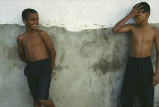 TANZANIA, Zanzibar Island, Zanzibar, Two wet boys wearing jeans leaning against wall and laughing