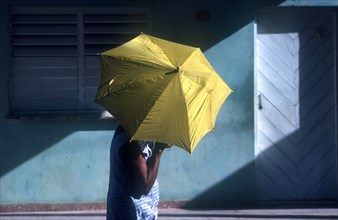 CUBA, Ciego De Avilar  , Woman with yellow umbrella as sun shade in the street