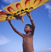 INDONESIA, Lombok, Timur, Young boy holds up a yellow eagle shaped kite