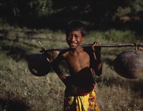 INDONESIA, Lombok, Timur, Mawon near Kuta a young boy in floral sarong holding pole of dried