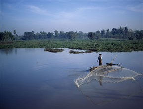 INDONESIA, Lombok, Timur NTB, "Praya, man fishing from outrigger canoe using circular casting net,