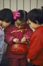 CHINA, Sichuan Province, Chengdu , Three young Chinese children looking in handbag wearing red and
