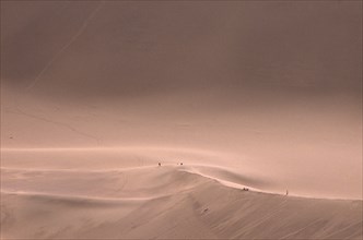 CHINA, Gansu, Dunhuang, Sand dunes with people standing on the ridge in the distance