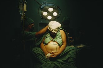 CUBA, Havana, Woman in labour sitting on an operating table with doctors at her sides