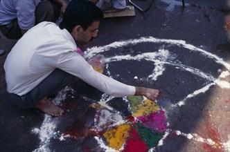 INDIA, Delhi , Man painting wheel-like design on the ground to be used as a base for a bonfire