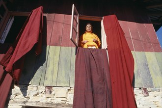 INDIA, Sikkim, Pemayangste Monastery, Buddhist Lama standing at a window with drapes hanging from