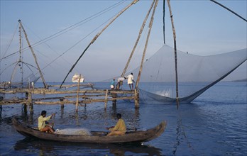 INDIA, Kerala, Kochi, Chinese fishing net being raised with a catch as two men row past in a canoe