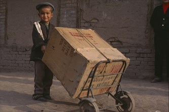 CHINA, Xinjiang, Kashgar , Child pushing a box on two wheeled trolley