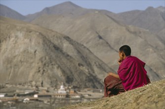 CHINA, Gansu, Xiahe , Tibetan Monk sitting on hillside overlooking Xiahe Monastery