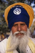 INDIA, Delhi, "Portrait of a sikh man wearing orange and royal blue  turban set with a khanda, the