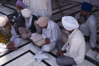 INDIA, Punjab, Amritsar, Group of Sikh men reading from holy book on black and white marble floor