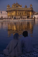 INDIA, Punjab, Amritsar, Sikh couple sitting on marble walkway looking out across sacred pool