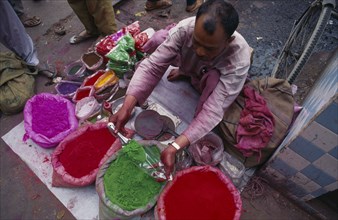 INDIA, Delhi, Street trader measuring out brightly coloured Holi Festival paints.