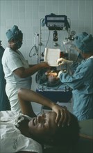 CUBA, Havana, Woman lying with her hand on her head after giving birth while two nurses weigh her
