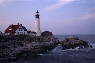 USA, Maine, Portland, Portland Head Lighthouse. Waves crashing against rocks seen at dusk in warm