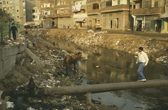 EGYPT, Damietta, Nile Delta, Rubbish in canal with man walking over pipe