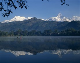 NEPAL, Pokhara, Phewa Lake with mountain peak reflected. Men in boat and branches in the foreground