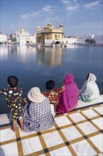 INDIA, Punjab, Amritsar , Women and children sitting on walkway beside sacred pool looking across