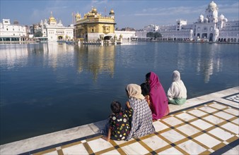 INDIA, Punjab, Amritsar, Three women and children sitting on marble walkway beside the sacred pool