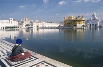 INDIA, Punjab, Amritsar , Sikh man sitting on marble walkway beside the sacred pool surrounding the