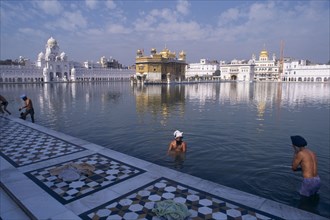 INDIA, Punjab, Amritsar , Golden Temple. Men bathing in the sacred pool surrounding the temple.