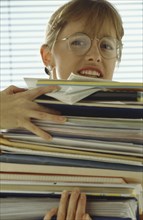 BUSINESS, Paperwork, Female office worker with stressed expression weighed down with stack of