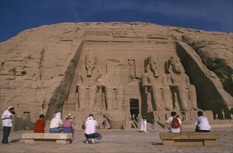 EGYPT, Abu Simbel, Tourists sitting in front of giant seated statues of Ramesses II at temple