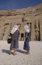EGYPT, Abu Simnel , Two female tourists wearing head scarves in front of staues of Ramesses II at