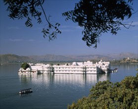 INDIA, Rajasthan, Udaipur, The Lake Palace framed by tree branches with white reflections on water