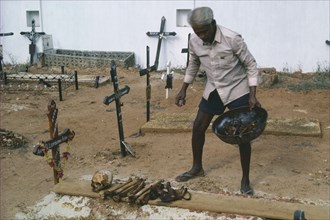 INDIA, Goa, Colva, Man cleaning bones at family grave. The bones are removed and washed to make