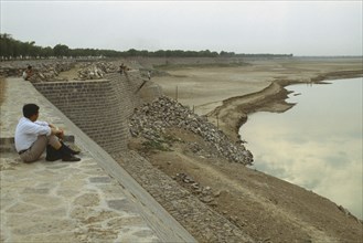 CHINA, Jinan, Yellow River, Yellow River Dykes with man sat on ground looking towards water