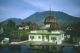 INDONESIA, Sumatra, Mosque with rusty tin domes by a lake with people sitting at the waters edge
