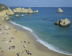 PORTUGAL, Algarve, Lagos, "Sandy beach, outcrops of rocks in sea, family groups "