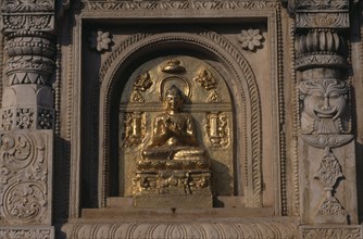 INDIA, Bihar, Bodhgaya, Buddha image carved in golden section of niche in wall.