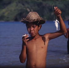 INDONESIA, Lombok, Mawon, "Boy smoking cigarette, hat, small fish on line "