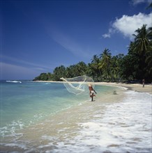 INDONESIA, Lombok, Mentiggi, Fisherman casting fishing net into sea from the surf on a coconut palm