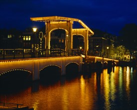 HOLLAND, North, Amsterdam, Magere Brug or Skinny Bridge illuminated at night with lights reflected