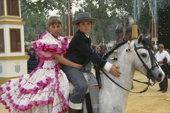 SPAIN, Andalucia, Jeréz de la Frontera, Children in flamenco costume on a grey pony at Jerez horse