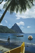 WEST INDIES, St Lucia, Soufriere, Man walking along beach with boats moored offshore and the Pitons